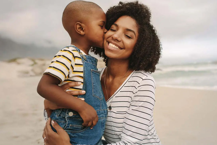 Individual Life Insurance Young Son Kissing His Smiling Mother While Being Held at the Beach on a Cloudy Day